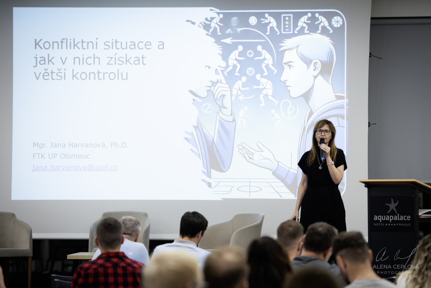 Jana Harvanová přednáší na konferenci Psychologie sportu v praxi, na plátně za ní je název přednášky Konfliktní situace a jak v nich získat větší kontrolu