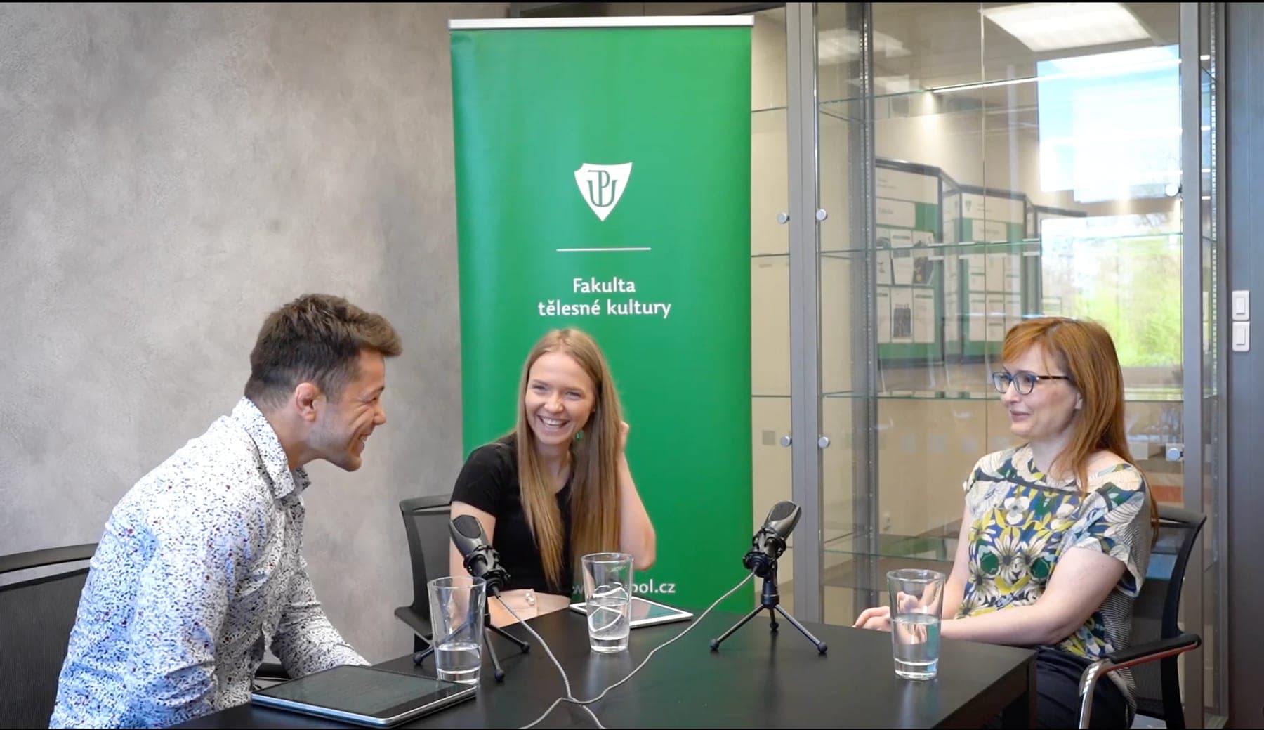 Natáčení Vrcholového podcastu: Jana Harvanová s moderátorskou dvojicí u mikrofonů před bannerem FTK UP